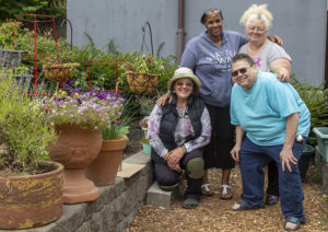 Four gardeners smile next to a flourishing garden.