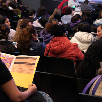 The backs of people seated in chairs facing a stage