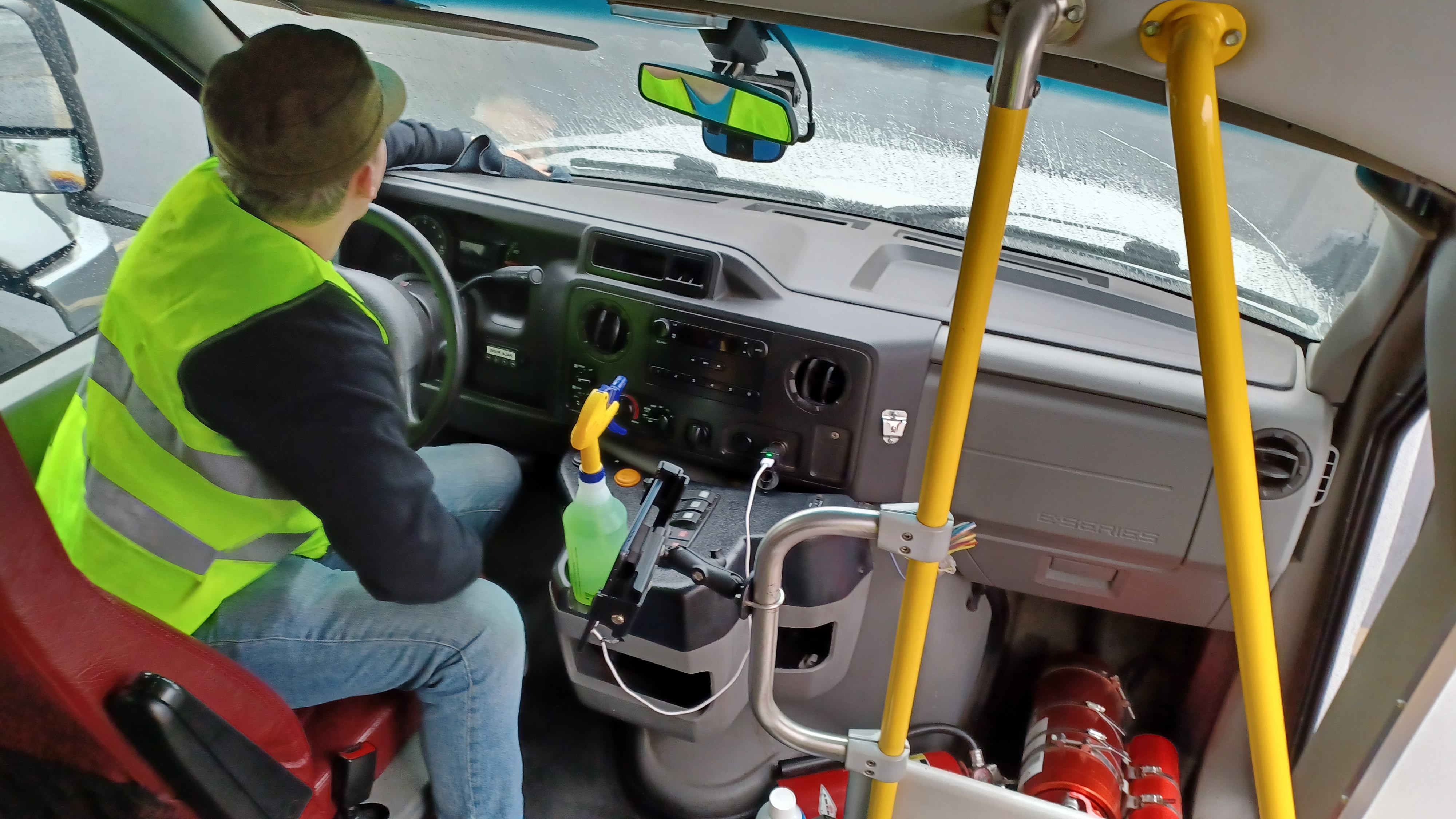 A man sitting in the driver's seat of paratransit bus cleans the drivers area