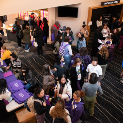 An overhead shot of a hallway outside a door labeled "orchestra level" crowded with people chatting in groups.
