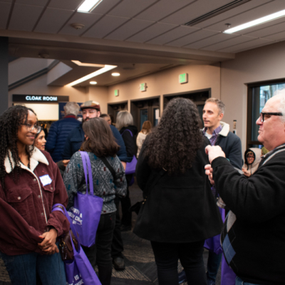 People mill about in a room with windows facing a street.