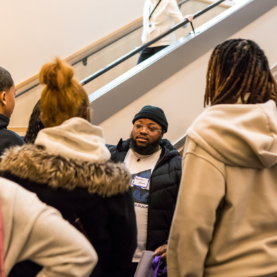 A man stands in front of a staircase as others face him.