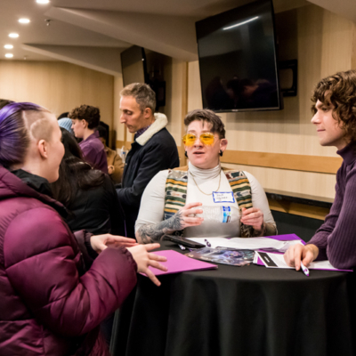 A person in amber-colored glasses speaks as two others listen.