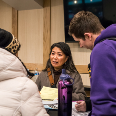 A woman with long dark hair speaks as two others listen.