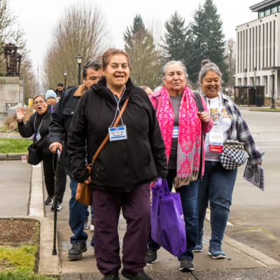 Several people smile as they lead a group down a sidewalk.