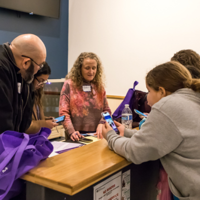 Several people lean over a desk looking at their phones.