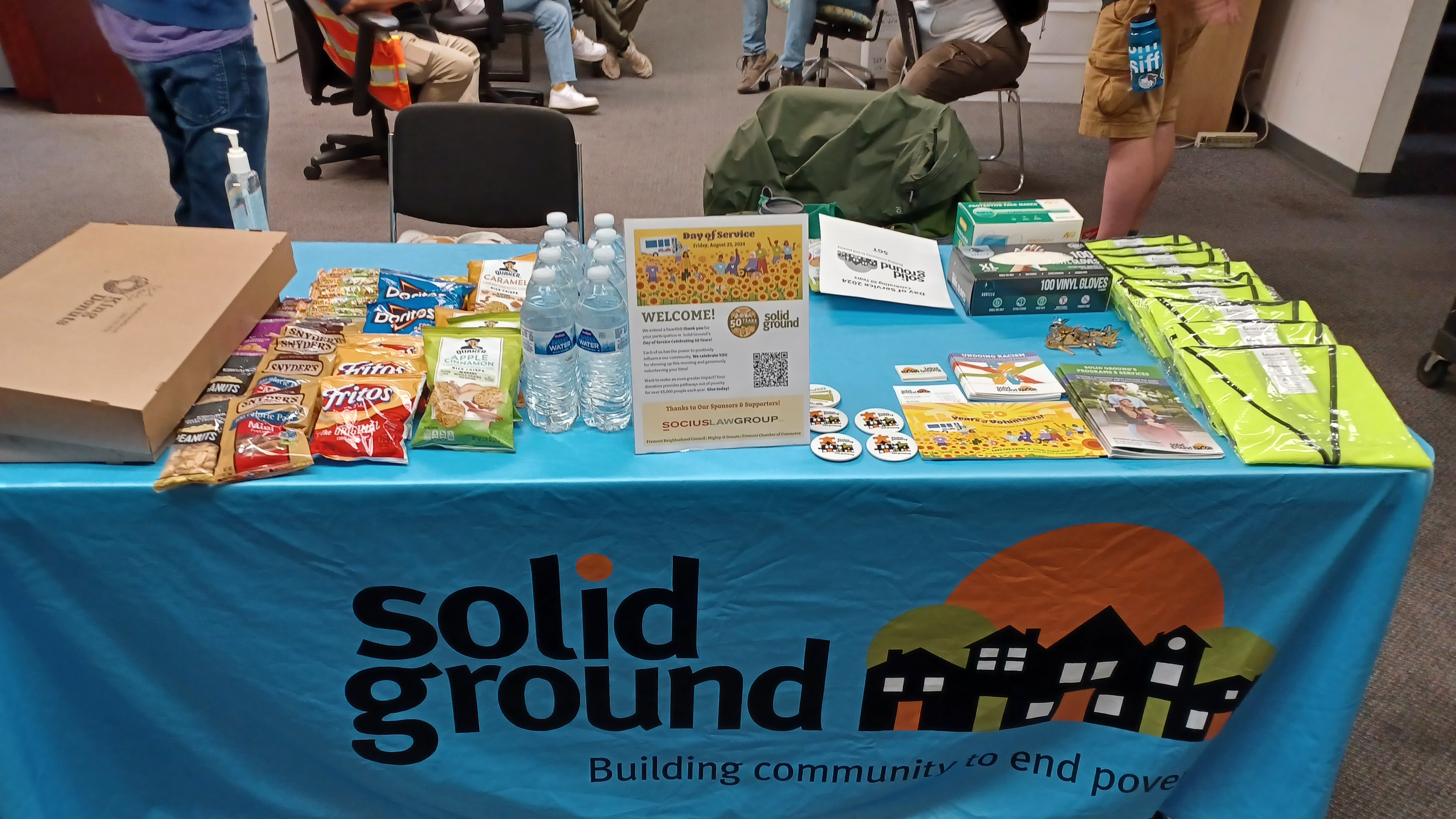 A table covered with a blue Solid Ground table cloth a long with stickers, snacks, and other items for volunteers.