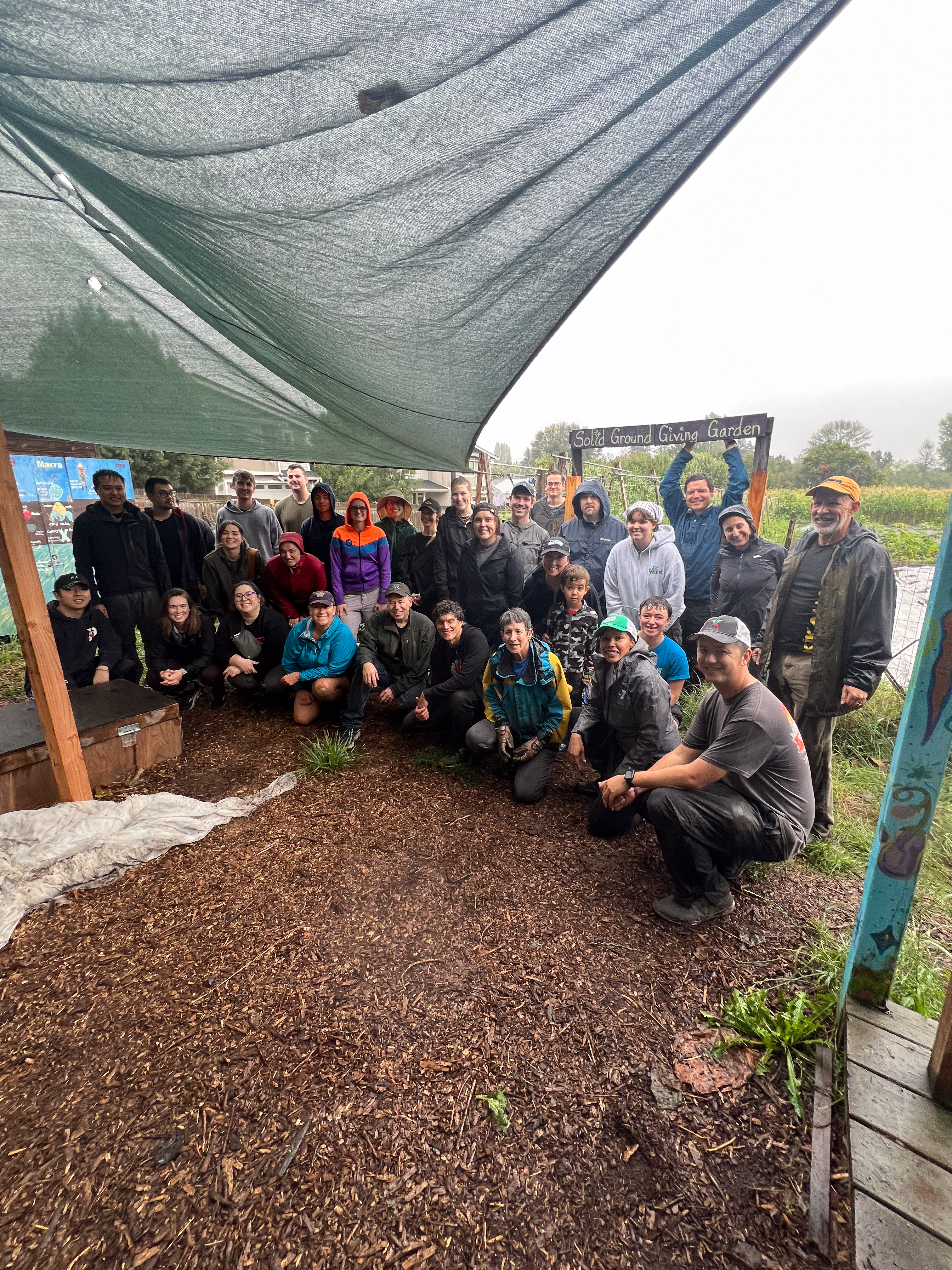 A group of people, some of them squatting down, pose for a picture under a tarp.