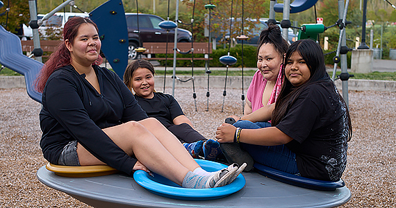 A mom and three youth/teen kids pose together on a playground.