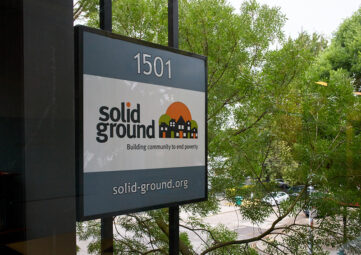 A sign on the side of a building that reads "Solid Ground - Building Community to Solve Poverty."
