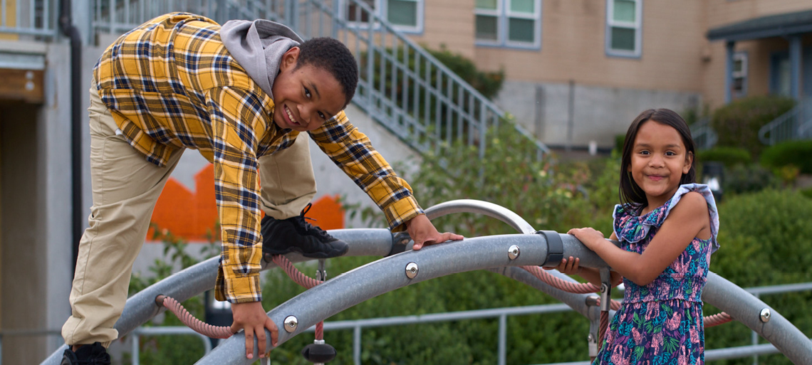 Two middleschoolers smile at the camera while playing on a jungle gym.