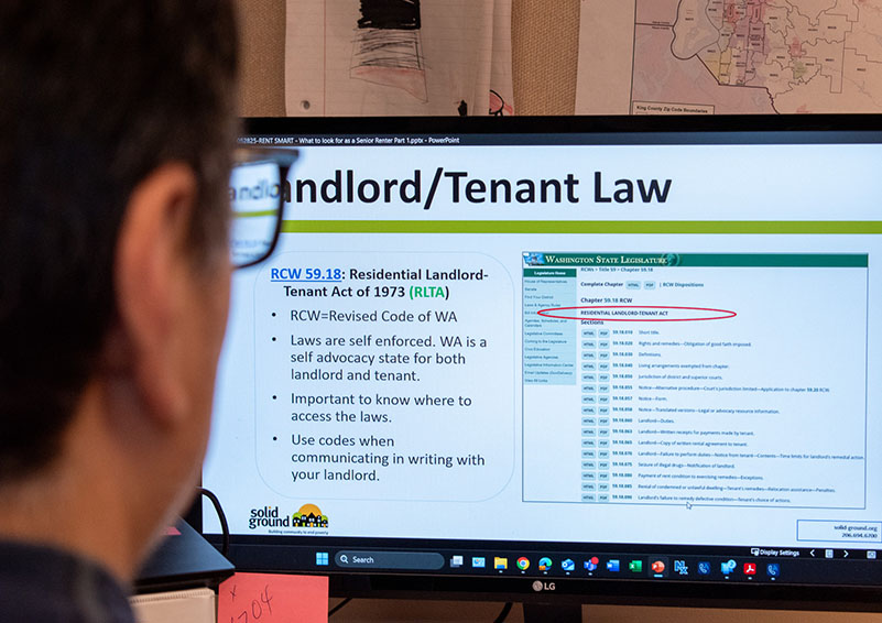 Man with dark hair and glasses, wearing a dark blue plaid shirt, sit facing a computer screen with a PowerPoint presentation up that reads, "Landlord/Tenant Law."