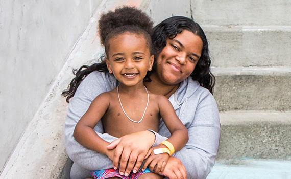 A mom hugs her son. They're sitting on a set of concrete steps.