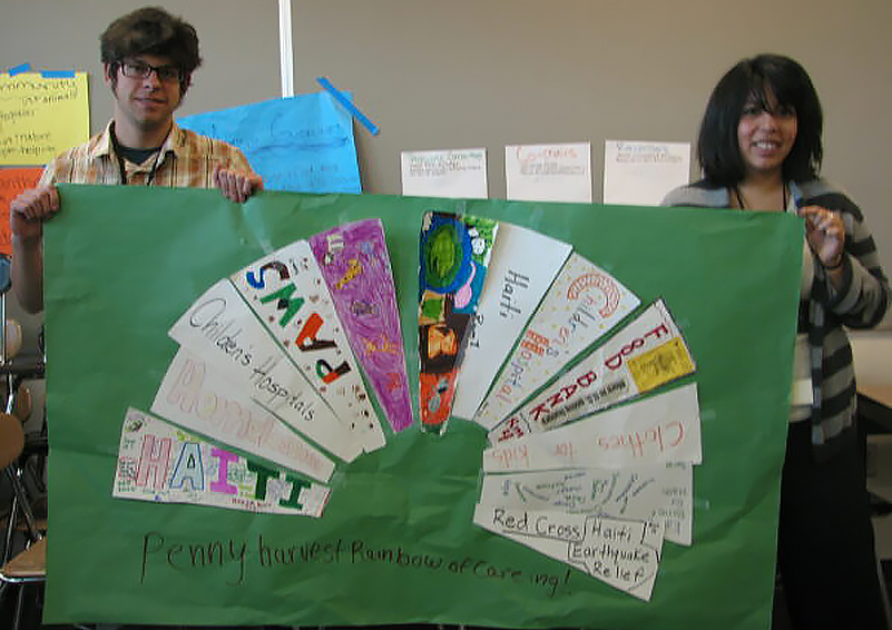 Two people hold up a large green display with a "Rainbow of Caring" on it.