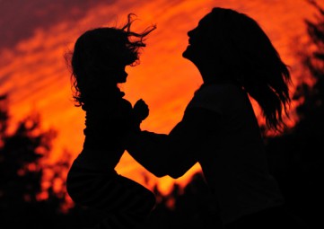 Silhouette of a mother lifting her young daughter joyfully with a bright orange sky behind them