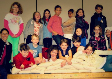 A group of 16 elementary school students and one teacher pose with a mound of sacks filled with coins.