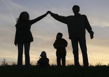 silhouette of a family with two adults forming a roof over the heads of two children at sunset
