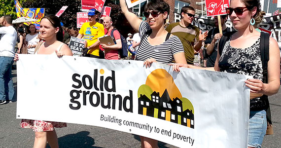 People marching in a crowd holding a Solid Ground banner