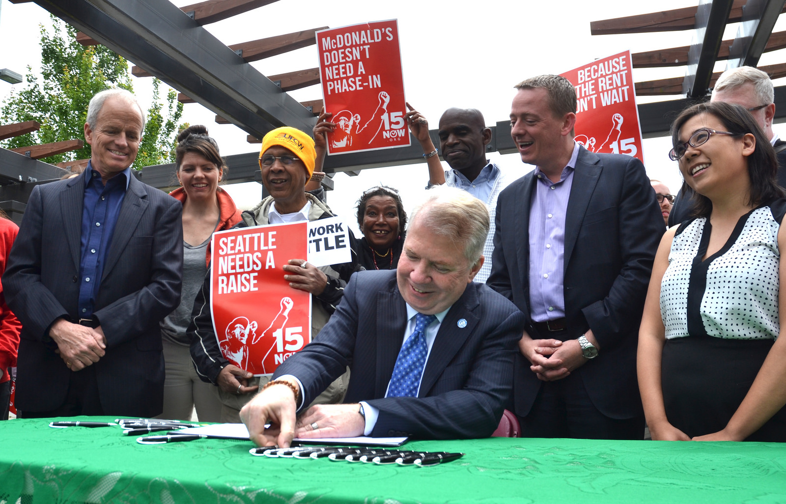 Seattle Mayor Ed Murray signs $15 minimum wage into law as Gordon McHenry, Jr. (5th from left) looks on. (Photo from murray.seattle.gov)