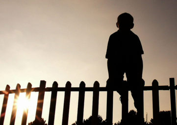 silhouette of boy climbing a fence