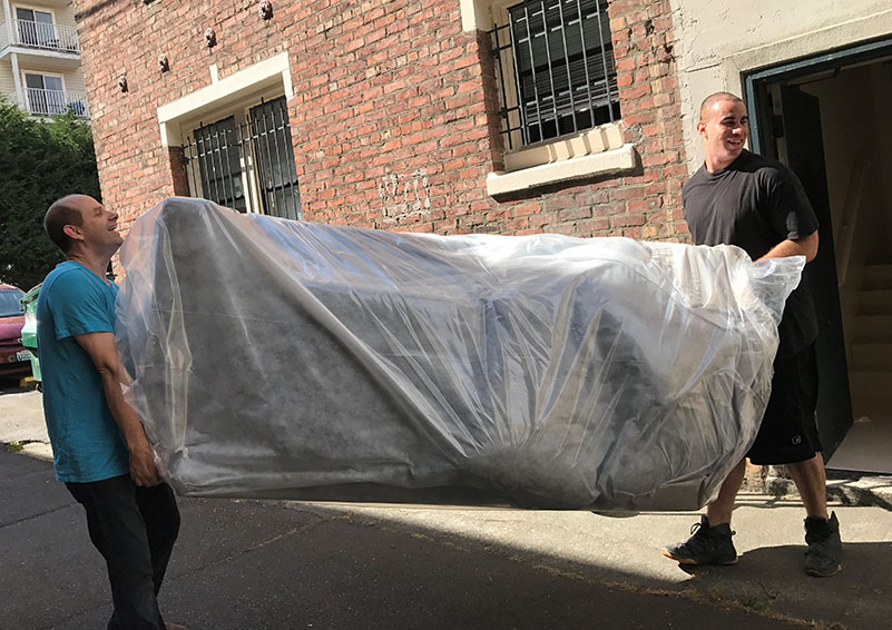 Josh Underhill, left, carries one of 31 new sofas into Broadview with his staff members.
