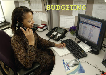Budgeting: Woman on the phone at her computer takes notes on a notepad