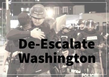 Police and protester hug under banner that says De-Escalate Washington