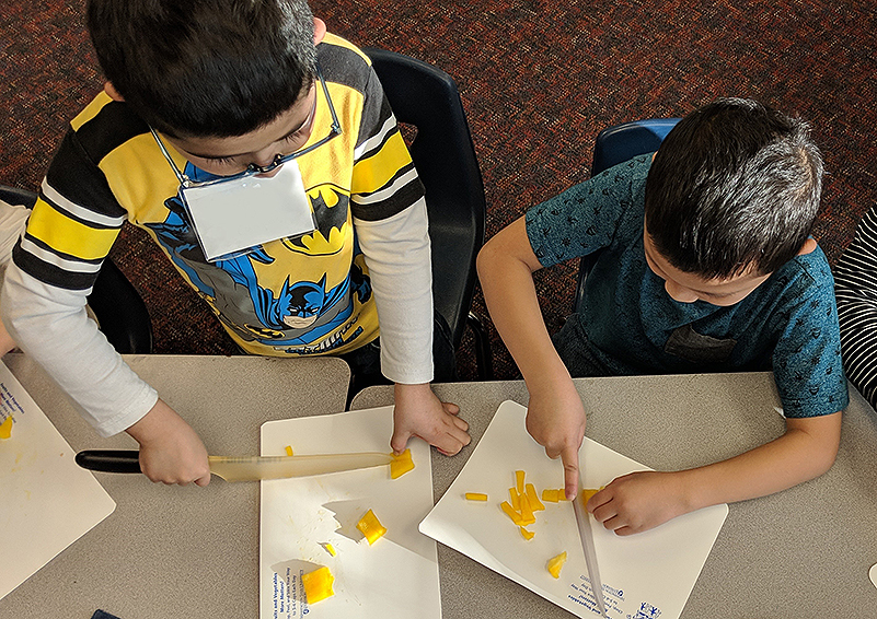Students in afterschool cooking club practice their knife skills on yellow bell peppers for a mango salsa recipe. (Photo by Emiline Chipman)