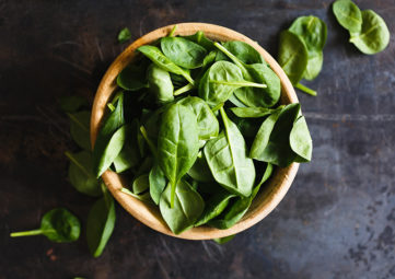 Wooden bowl filled with fresh spinach on a black counter