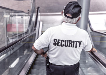 A white-haired security guard with black cap takes the escalator