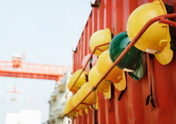 Hard hats hanging on the side of a storage container, with a tower crane in the background