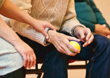 A women gently holding the wrist of an elderly man holding a ball