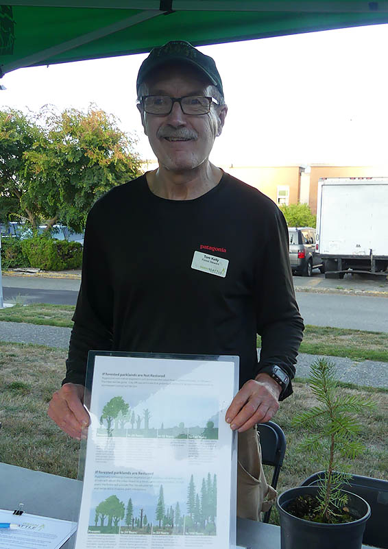 Man holds up a graphic of trees at the Green Seattle table.