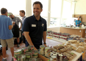 Andy Sharpe, Executive Director of the University Family YMCA, smiles in front of a canned goods displayon opening day of the Magnuson Park Community Food Pantry