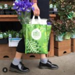 Person walking with a Whole Foods Market shopping bag with purple lilies in it