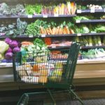 Whole Foods Market shopping cart with groceries in front of a display of veggies