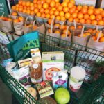 Whole Foods Market shopping cart with groceries in front of a display of oranges