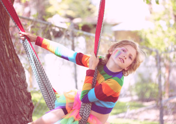 Child in rainbow clothing swinging from a hammock