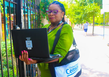 African-American woman with purple glasses and a green top with a 2020 US Census bag and laptop