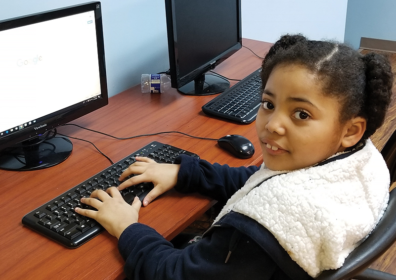 Young girl sits at a computer in the Sand Point Housing computer lab.