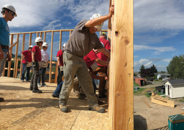 Habitat for Humanity volunteers in hard hats put up wood frame for a 2-story house