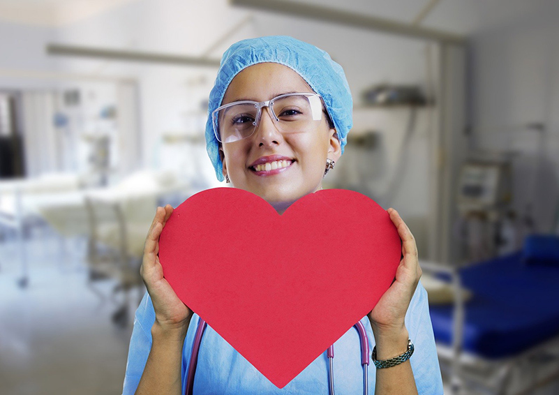 A nurse in blue scrubs holds a red paper heart in her hands