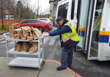 Access bus driver pushing cart with brown bags containing food
