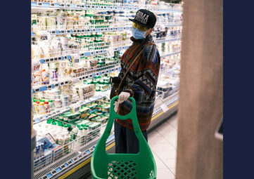 Asian woman in mask, cap & gloves shops at a grocery store