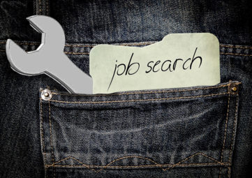 Graphic of the back pocket of charcoal gray jeans with gold stitching. A wrench and a slip of paper with "job search" on it is sticking out of the pocket.