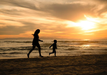 Silhouetted image of mother and child running on the beach during a sunset.