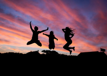 Silhouette image of three kids jumping for joy in front of sunset.