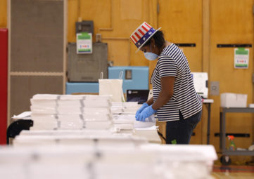 poll worker in "Uncle Sam" flag hat prepares paper ballots