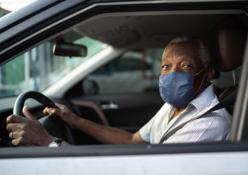 immigrant man wearing a blue mask sits in his car