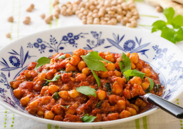 blue and white bowl with black spoon, filled with orange garbanzo beans, chana masala